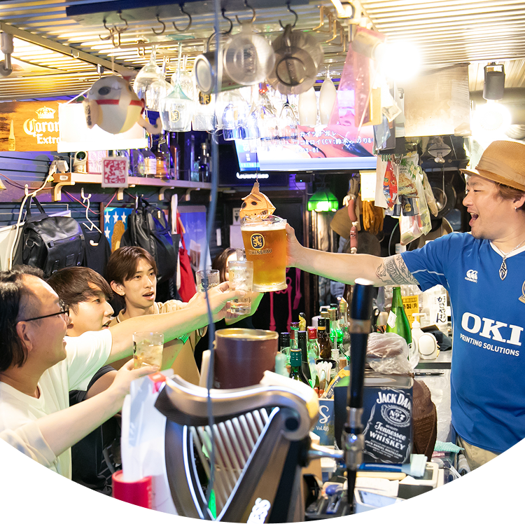 カウンターでグラスを掲げて乾杯するお客さんと店長